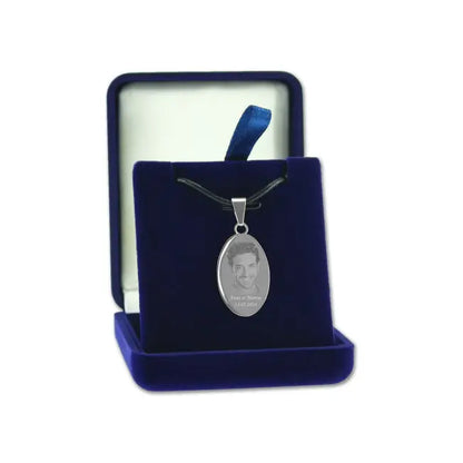 Pendentif ovale en finition argent avec photo gravée, présenté sur un cordon noir dans un écrin bleu velours ouvert.