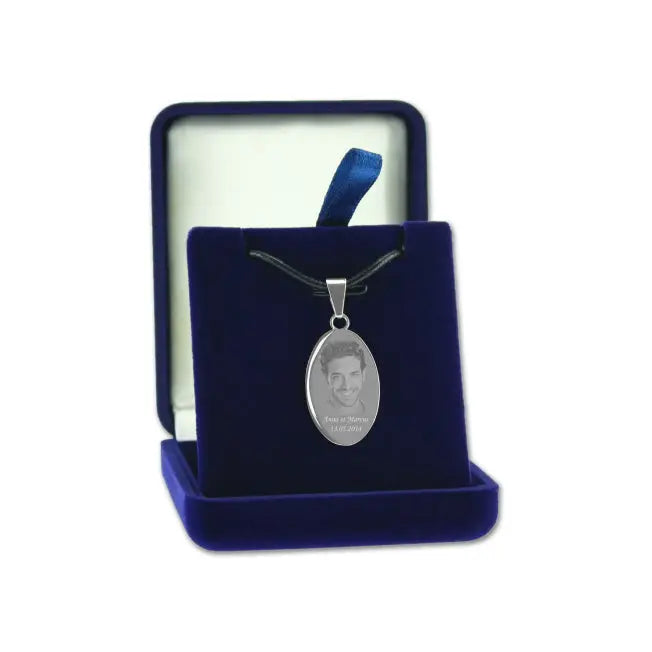 Pendentif ovale en finition argent avec photo gravée, présenté sur un cordon noir dans un écrin bleu velours ouvert.
