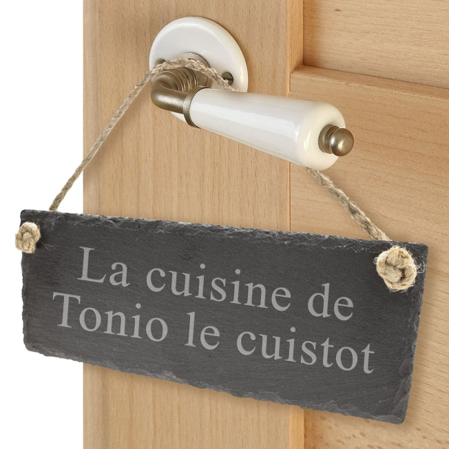 Plaque de porte en ardoise personnalisée, gravée avec « La cuisine de Tonio le cuistot », suspendue à une poignée de porte.
