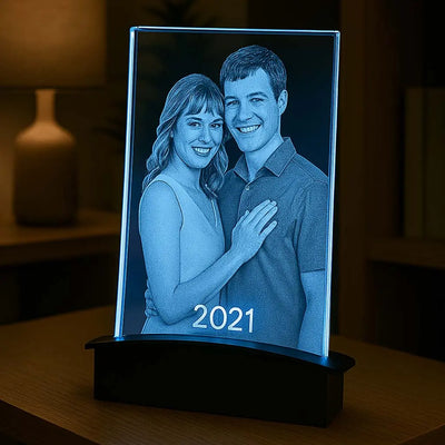 Plaque en verre rétroéclairée en bleu par un socle tunnel LED. Le couple souriant et l’année gravée ressortent parfaitement dans un décor chaleureux.