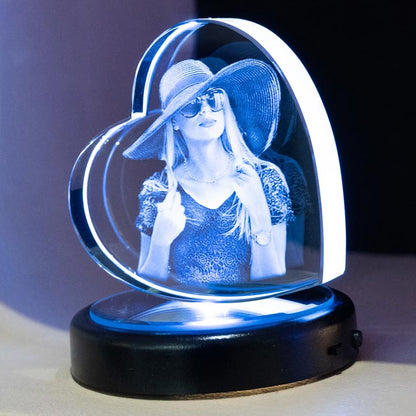 Une jeune femme avec un chapeau est gravée en 3D dans un bloc en forme de cœur en verre. Cadeau personnalisé original et raffiné avec socle lumineux.