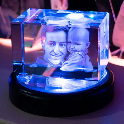 Un père tient son bébé dans un bloc en verre allongé, gravé en 3D et posé sur un socle lumineux. Ce bloc personnalisé est idéal pour la fête des pères ou une naissance.
