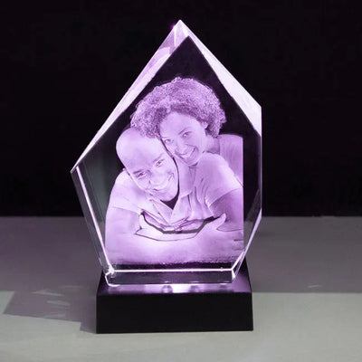 Trophée en verre Prestige 16 cm avec gravure 3D d’un couple enlacé, sublimé par une lumière violette de son socle lumineux. Cadeau personnalisé idéal.